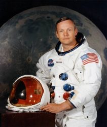 Portrait of Astronaut Neil Armstrong in his space suit, with his helmet on the table in front of him. 1969. (Via Wikipedia)